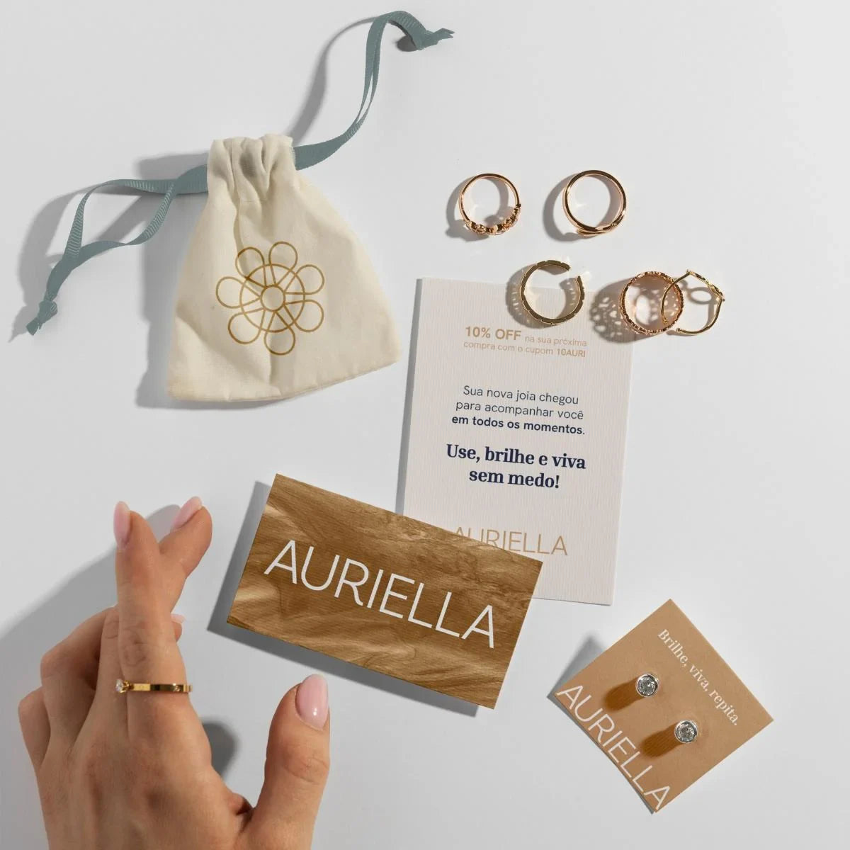 Gold rings, stud earrings, and branded cards arranged with a jewelry pouch on a white surface